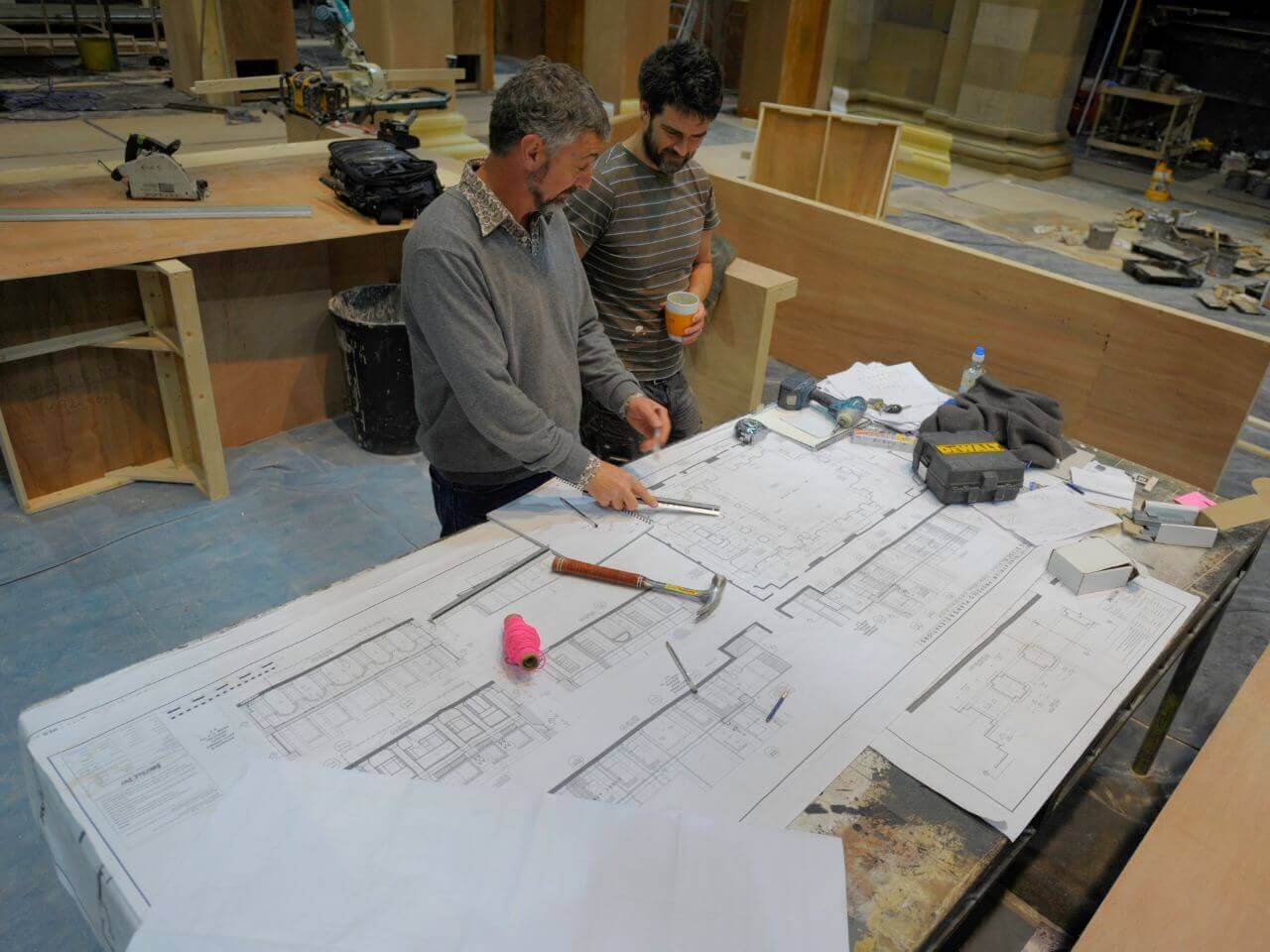 Tom & Designer with Drawings - The Take Set Tom Overton and a designer reviewing detailed set drawings on the workshop floor for The Take.