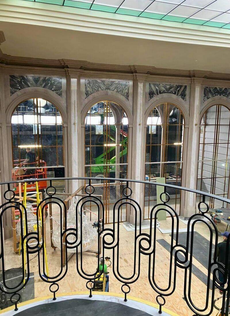 Man vs Baby - Double-Height Ceiling and Roof Light Construction crew installing flooring beneath the large double-height arched windows of the penthouse set, with the studio and rigging visible behind the glass.