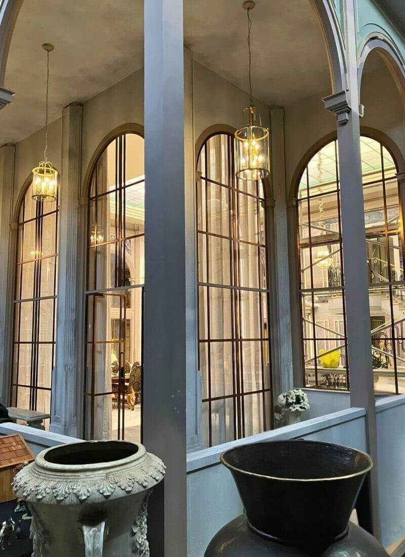 Man vs Baby - Double Height Windows - View from Balcony outside View from the exterior balcony side of the set, showing the tall arched windows, gold glazing bars and hanging pendant lights, with the main living space visible through the glass.