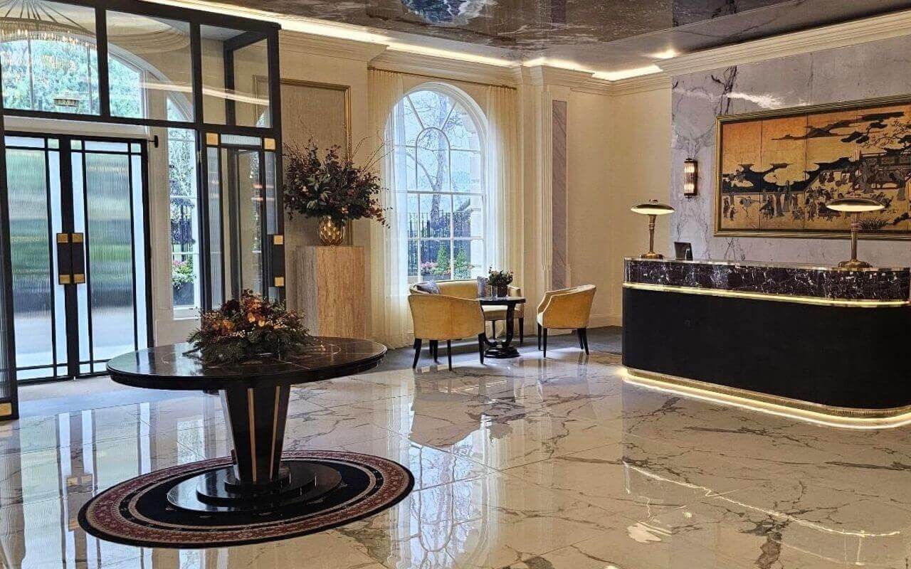 Man vs Baby - Lobby Set – St James Interior Recreation Dressed lobby set with marble flooring, ribbed glass doors, seating area and a dark marble reception desk.
