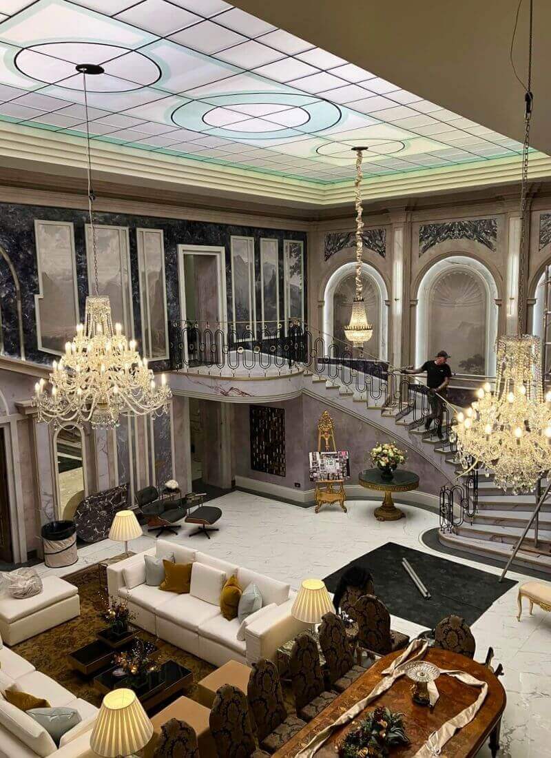 Man vs Baby - Main Living Room and Staircase – Full Set View High-angle view of the completed penthouse set showing chandeliers, staircase, sofas and the acrylic roof light.