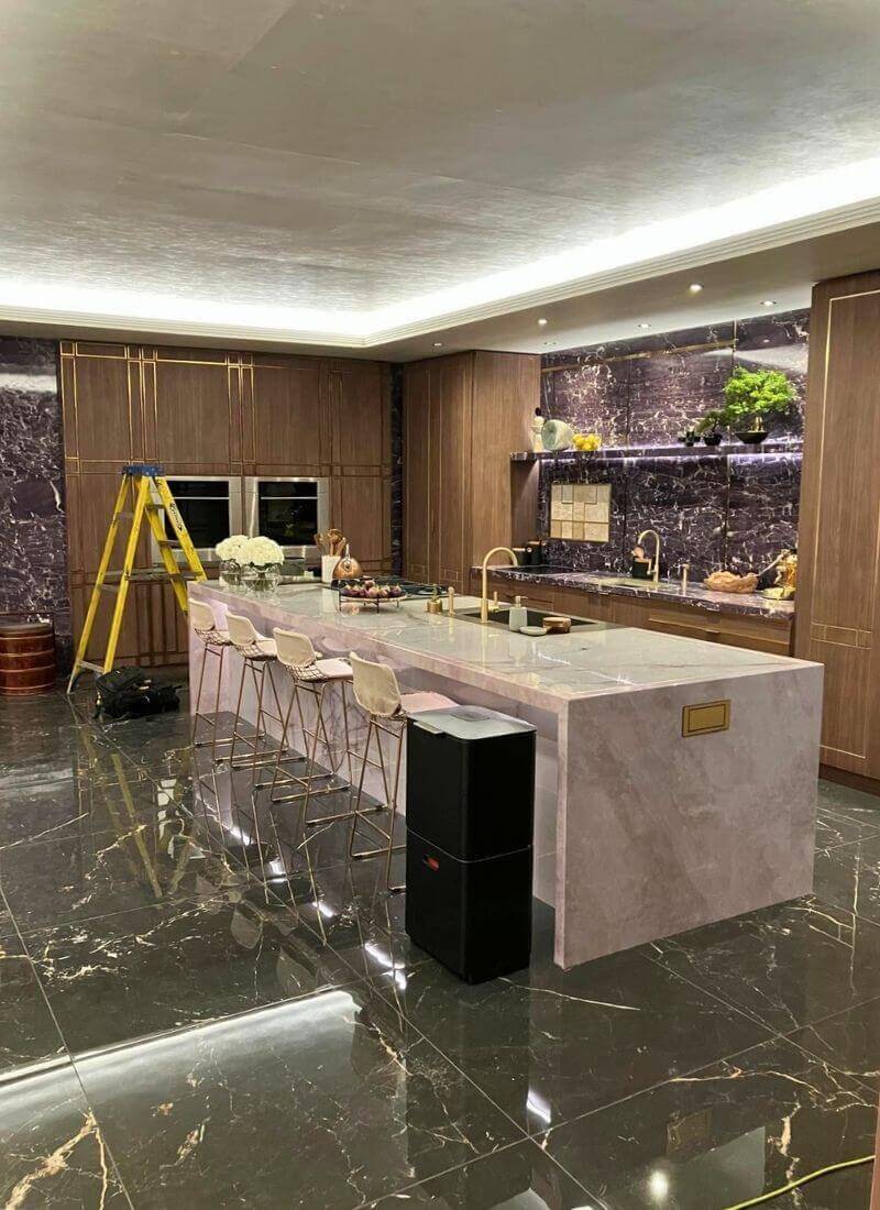 Man vs Baby - Penthouse Kitchen – Completed Set Wide view of the finished kitchen set with dark stone-effect walls, large marble island and warm timber cabinetry.