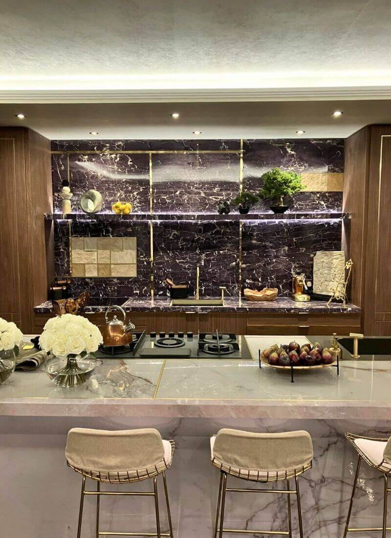 Man vs Baby - Penthouse Kitchen – Scenic Stone and Gold Detailing Dressed kitchen area with dark stone-effect wall panels, gold trim, shelving, and decorative items on the Man Vs Baby set.